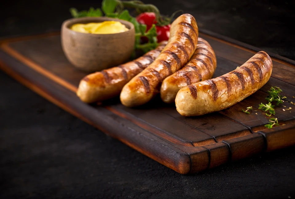 Saucisses grillées artisanales disposées sur planche à découper en bois, accompagnées de moutarde en pot céramique et herbes fraîches, présentation gastronomique professionnelle