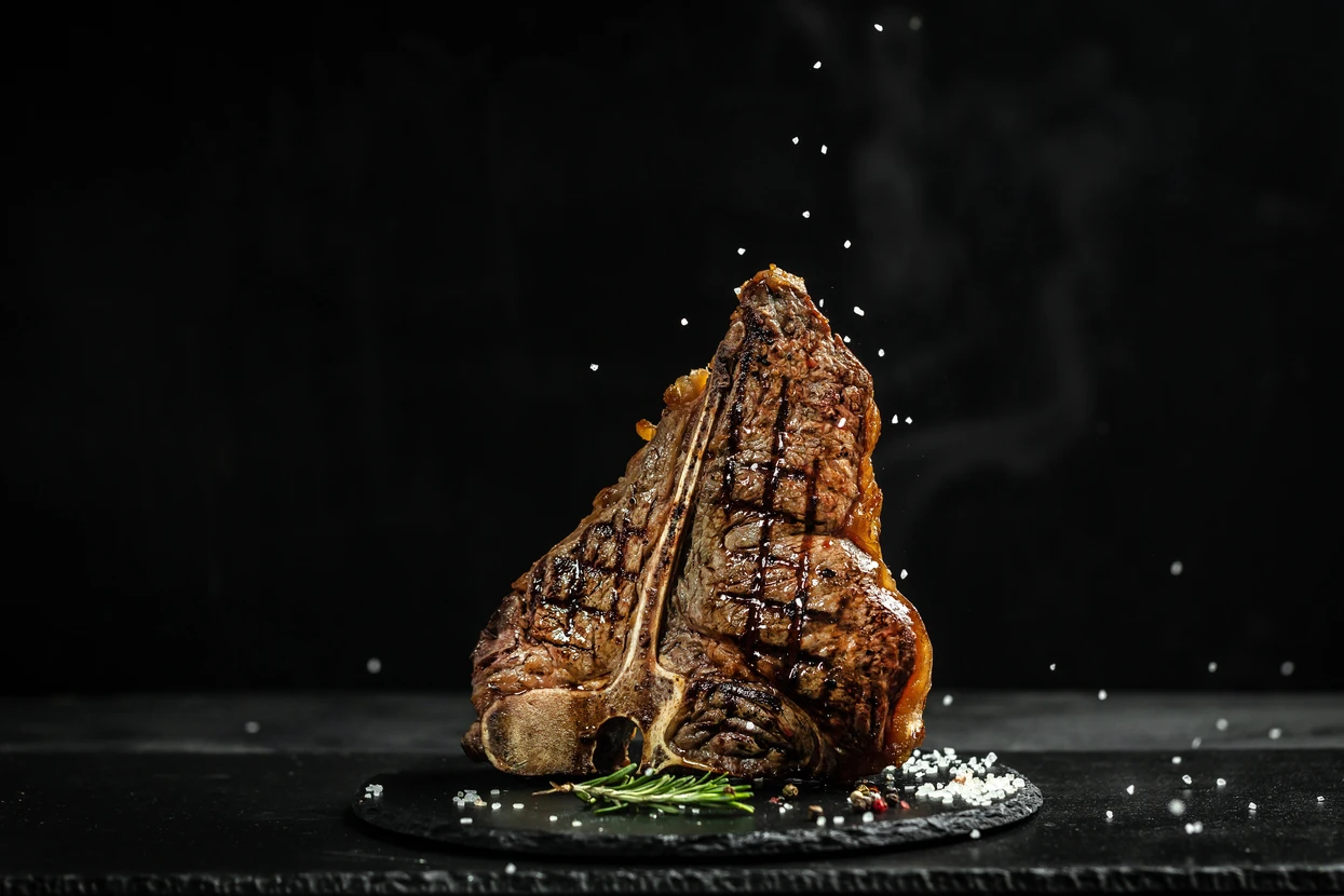 Côte de bœuf grillée sur planche d'ardoise noire avec grains de sel et brin de romarin frais