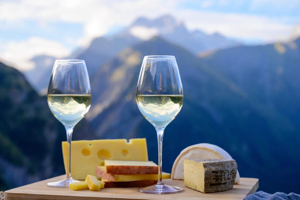Scène extérieure de dégustation en montagne avec deux verres de vin blanc et plateau de fromages artisanaux sur table en bois