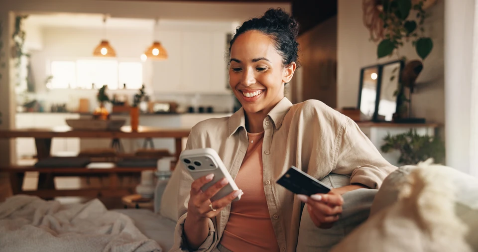 Personne effectuant un achat en ligne sur ordinateur portable, tenant une carte bancaire rouge dans la main gauche tout en tapant sur le clavier de la main droite