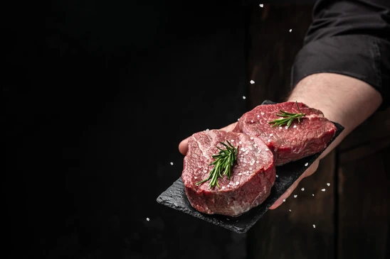 Plat de service présentant un rôti de porc farci tranché, garni de romarin frais sur assiette beige