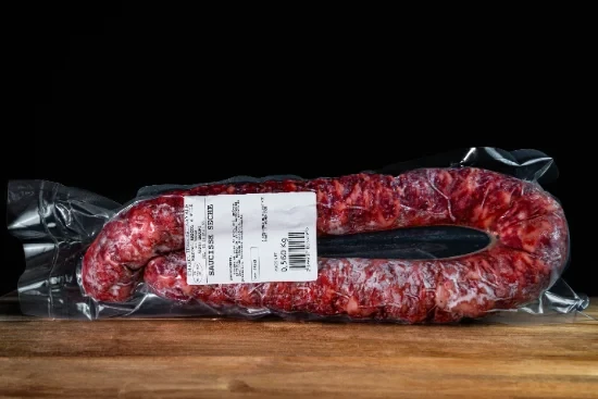 Saucisses grillées artisanales disposées sur planche à découper en bois, accompagnées de moutarde en pot céramique et herbes fraîches, présentation gastronomique professionnelle