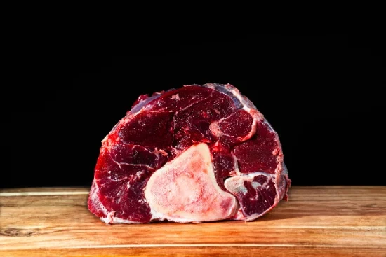 Scène conviviale de dégustation gastronomique avec personne tenant un verre de vin rouge au-dessus d'une table garnie de charcuteries, fromages, olives et cornichons disposés sur planches de bois