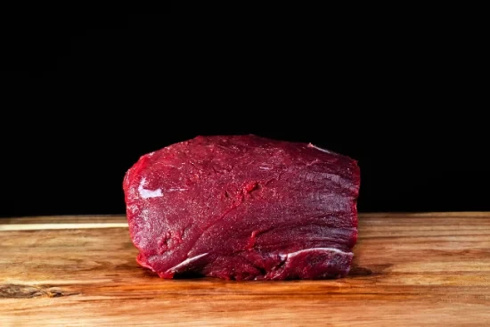 Scène conviviale de dégustation gastronomique avec personne tenant un verre de vin rouge au-dessus d'une table garnie de charcuteries, fromages, olives et cornichons disposés sur planches de bois