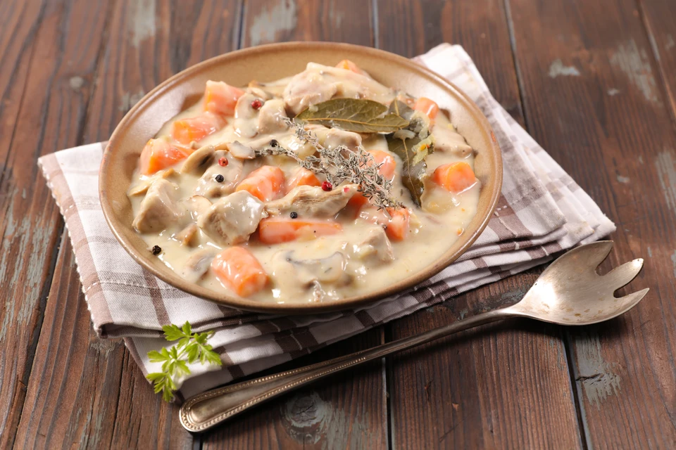 Photographie d'un plat cuisiné savoureux et appétissant présenté dans une assiette blanche sur un fond de cuisine professionnelle ou table rustique. Le plat doit mettre en avant une viande artisanale de qualité (rôti, côte, pavé ou préparation traiteur traditionnelle) accompagnée de légumes de saison, dans un style culinaire traditionnel français. La photo doit transmettre l'authenticité, le soin apporté à la préparation et l'appétit, sans texte ni logo visible.